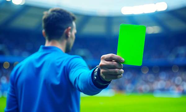 Sinipaitainen erotuomari näyttää vihreää korttia kohti katsojaa – kuva symboloi suomalaispelaajien verovapaita voittoja ETA-lisensoiduilla nettikasinoilla.